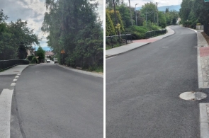 Ulica w Cieszynie po modernizacji, z nową nawierzchnią asfaltową i chodnikami z kostki brukowej. Otoczona zielenią i zabudową jednorodzinną, z barierkami ochronnymi, oznakowaniem i widokiem na góry w tle.