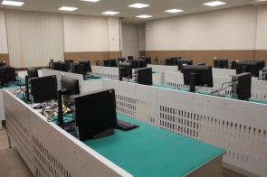 Nowoczesna sala komputerowa z równymi rzędami stanowisk; monitory ustawione na zielonych blatach, jasne oświetlenie i żaluzje w oknach - sala ZST w Ustroniu.