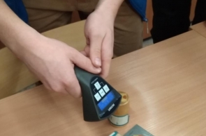 Uczeń trzyma smartfon nad ilustracją przedstawiającą obiekt 3D, ustawioną na ławce w klasie.