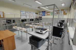 Pracownia techniczna z metalowymi stanowiskami roboczymi; na stołach monitory, sprzęt komputerowy i projektor, po lewej biurko nauczyciela - sala ZSTiO w Skoczowie.