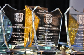  Szklane statuetki z wyrytymi napisami "Nagroda Powiatu Cieszyńskiego" dla wyróżnionych osób za wysokie osiągnięcia sportowe w 2023 roku. W tle widać złote elementy dekoracyjne.