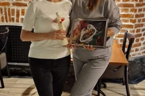 Dwie kobiety pozują przy ceglastej ścianie we wnętrzu lokalu – z prawej Marta Tabaka, z lewej jej siostra bliźniaczka. Siostra Marty trzyma ceramiczną figurkę kobiety w białej sukni z czerwonym sercem, Marta – obraz z motywem dłoni i serca. Obie uśmiechnięte, stoją blisko siebie w przyjacielskim geście.