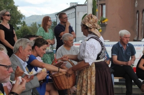 Starosta cieszyński Janina Żagan, w tradycyjnym stroju ludowym rozdaje pieczywo uczestnikom Dożynek Powiatowo-Gminnych w Goleszowie, siedzącym na ławkach podczas plenerowego święta.