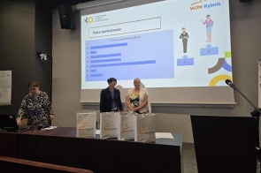 W sali konferencyjnej, przed ekranem z prezentacją „Prace konkursowe – Liczba uczestników konkursu” (logotypy: Kuratorium Oświaty w Katowicach i WOM Rybnik), stoją dwie uśmiechnięte kobiety z identyfikatorami. Po lewej stronie trzecia osoba obsługuje laptop.