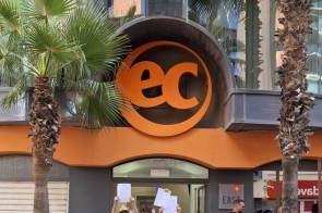 Duża grupa młodzieży z opiekunami pozuje przed nowoczesnym budynkiem z dużym pomarańczowym logo „EC”, między palmami. Wszyscy uśmiechnięci, trzymają w górze certyfikaty.