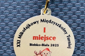 Medal zawieszony na niebiesko-białej wstążce, z napisem informującym o pierwszym miejscu w XXIX Mikołajkowym Międzyszkolnym Turnieju w Bielsku-Białej w 2025 roku, ozdobiony ilustracją Mikołaja i renifera.