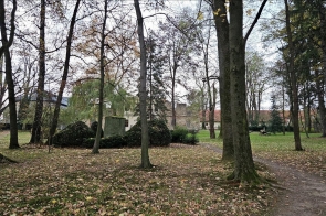 Fragment dawnego parku dworskiego, w tle ruiny Dworu Kossaków, z lewej strony w głębi Spichlerz Dworski odrestaurowywany przez inwestora Powiat Cieszyński (06.2023–10.2025), z prawej strony w głębi Hostel „KOSS”, wśród drzew i parkowej zieleni.