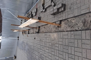 Chodnik z kostki brukowej w trakcie robót budowlanych. Przez środek biegnie wykop, obok ułożone kostki. Nad wykopem zamontowane są prowizoryczne drewniane kładki, po bokach metalowe ogrodzenie.