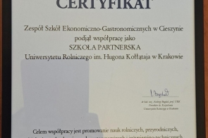 Certyfikat w czarnej ramie z nagłówkiem „CERTYFIKAT” oraz herbem u góry. Treść informuje o podjęciu współpracy przez Zespół Szkół Ekonomiczno-Gastronomicznych w Cieszynie jako szkołę partnerską Uniwersytetu Rolniczego im. Hugona Kołłątaja w Krakowie. Na dole widoczna data „Kraków, 3 lutego 2026 r.” oraz podpis prorektora. Tło certyfikatu zawiera geometryczne wzory w odcieniach czerwieni, granatu i szarości.