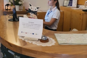 Kobieta z identyfikatorem na niebieskiej smyczy siedzi przy recepcji i pracuje przy komputerze. Na ladzie znajduje się kartka z informacją o stażu uczniowskim, a w tle widać drewniane wnętrze z dekoracjami i tabliczkę „Willa Zaolzie”.