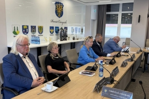 Radni podczas sesji siedzący przy stołach w sali sesyjnej. Na stołach widoczne są tablety, dokumenty, mikrofony, filiżanka kawy oraz tabliczki z nazwiskami