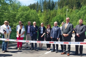 Grupa osób stojących na jezdni za rozciągniętą wstęgą. Część uczestników ubrana jest w stroje regionalne, pozostali w stroje formalne.