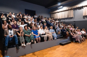 Na widowni sali widowiskowej siedzą uczestnicy wydarzenia. Publiczność zajmuje miejsca na kilku poziomach trybun i obserwuje program odbywający się poza kadrem.