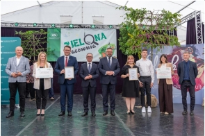 Grupa osób stoi na scenie podczas wydarzenia. Dwie osoby trzymają dyplomy i tablicę z napisem „Zielona Pracownia”. W tle widoczny jest baner wydarzenia oraz elementy scenografii.