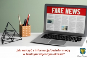 Na ekranie laptopa widoczny nagłówek „FAKE NEWS” na czerwonym tle, sugerujący tematykę fałszywych informacji. Obok komputerowego ekranu stoi pojemnik z długopisami i ołówkami oraz geometryczna dekoracja. U dołu grafiki widnieje pytanie: „Jak walczyć z informacją/dezinformacją w trudnym wojennym okresie?” oraz herb Powiatu Cieszyńskiego.