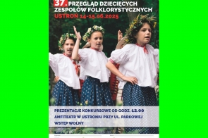 Trzy dziewczynki w tradycyjnych strojach ludowych, z wiankami na głowach i w białych bluzkach, tańczą i śpiewają na scenie otoczonej zielenią podczas festiwalu folklorystycznego w Ustroniu.