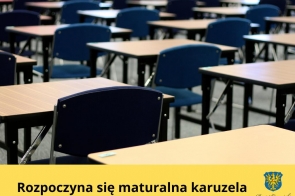Sala egzaminacyjna wypełniona pustymi, równomiernie ustawionymi ławkami i granatowymi krzesłami, przygotowana na rozpoczęcie egzaminów maturalnych. Na dole żółty pasek z napisem „Rozpoczyna się maturalna karuzela” oraz herbem Powiatu Cieszyńskiego.