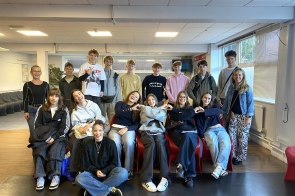 Siedemnaście uśmiechniętych młodych osób,dziewcząt i chłopców,pozujących w trzech rzędach.Sufit i ściany sali,na której się znajdują, są białe,a za nimi ściana jest mocno przeszklona.