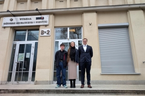 Troje młodych laureatów pozuje przed wejściem do Wydziału Inżynierii Mechanicznej i Robotyki. Eleganckie stroje, uśmiechy i duma w oczach podkreślają rangę wydarzenia, w którym właśnie wzięli udział.