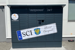 Urzędomat zlokalizowany przy budynku urzędu, oznaczony napisem „URZĘDOMAT 24/7”. Urządzenie ma ciemny kolor, z grafiką przypominającą tablicę rejestracyjną z napisem „SCI” i herbem Powiatu Cieszyńskiego.