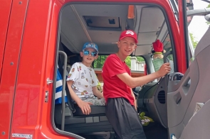 Dominik w stroju młodzieżowego strażaka zasiada za kierownicą wozu bojowego, a obok młodszy brat Bartek z uśmiechem i w stylowych okularach. Braterska drużyna gotowa na akcję – z sercem do ratowania i pasją do działania! 