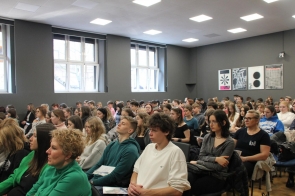 Młodzież i nauczyciele zasłuchani podczas konferencji w Sali konferencyjnej UŚ w Cieszynie. Pełne skupienia twarze, w tle nowoczesne wnętrze z dużymi oknami i plakatami na ścianie. Edukacyjne wydarzenie przyciągnęło liczne grono uczestników.