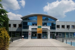 Nowoczesny budynek Zakładu Ubezpieczeń Społecznych (ZUS) z przeszkloną fasadą i charakterystycznym logo instytucji. Przed wejściem widoczna jest przestrzeń dla interesantów oraz elementy małej architektury.