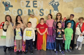 Grupa dzieci i dorosłych z Ośrodka Szkolno-Wychowawczego dla Niesłyszących i Słabo Słyszących w Raciborzu stoi przed kolorowym tłem z napisem „Dzień Godności”. Uczestnicy uśmiechają się, mają na sobie różnorodne, kolorowe stroje, a atmosfera jest radosna.