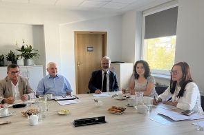 Zdjęcie przedstawia grupę sześciu osób siedzących przy dużym, jasnym stole w sali konferencyjnej. Od lewej siedzą: Janusz Żydek Wójt Chybia, Leszek Podżorski, właściciel firmy Wispol, Mieczysław Szczurek Wicestarosta, Anna Grygierek Burmistrz Strumienia, Magdalena Suchanek-Kowalska, Zastępca Burmistrza Strumienia. Uczestnicy spotkania siedzą wokół stołu, na którym znajdują się dokumenty.  