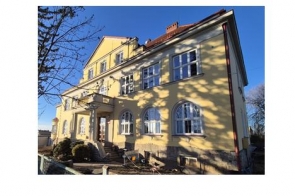 Jasnożółty, dwupiętrowy budynek z dużymi oknami w świetle słonecznym na tle błękitnego nieba.