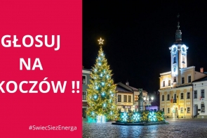 Na zdjęciu widoczny jest rynek w Skoczowie nocą, pięknie oświetlony świątecznymi dekoracjami. Centralnie stoi udekorowana choinka z gwiazdą na czubku, otoczona jasnymi, migoczącymi ozdobami w kształcie prezentów. W tle ratusz z podświetloną wieżą zegarową, dodający uroku tej zimowej scenerii.