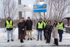 Grupa dziewięciu osób stoi na ośnieżonym poboczu drogi, pod tablicami informującymi o realizowanej inwestycji drogowej w ramach programu Interreg Polska–Słowacja oraz o prowadzonych pracach budowlanych. Wśród zebranych znajdują się przedstawiciele Powiatu i PZDP, wicewójt Istebnej oraz szef firmy Drogród. Część osób ma na sobie kamizelki odblaskowe, pozostali ubrani są w zimowe płaszcze i czapki. W tle widoczne są drzewa bez liści i zimowy krajobraz.