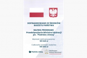   Informacja o programie dofinansowanym ze środków budżetu państwa. Program nosi nazwę "Podróże z klasą," realizowany przez Ministerstwo Edukacji Narodowej. Kwota dofinansowania wynosi 181 040 zł, a całkowita wartość zadania to 195 654 zł. Na górze widoczne są symbole Polski: flaga i godło.