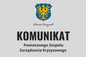 Herb Powiatu Cieszyńskiego oraz duży napis „KOMUNIKAT Powiatowego Zespołu Zarządzania Kryzysowego.” Grafika dotyczy ogłoszenia o charakterze informacyjnym dla mieszkańców powiatu.