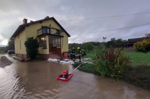 Strażacy wypompowują wodę z zalanej posesji przy domu jednorodzinnym. Woda sięga schodów wejściowych. Na pierwszym planie widoczna jest pompa.