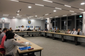 Sala sesyjna Powiatu Cieszyńskiego; stoły w „U”, kilkanaście osób, Janina Żagan - Starosta Cieszyński w białej koszuli przemawia. Na ścianie godło i herby gmin, na stołach filiżanki.