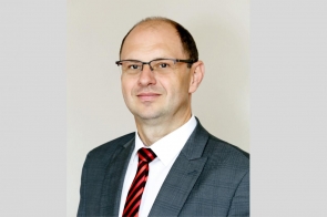 Nowy dyrektor Szpitala Śląskiego w Cieszynie Adam Śliż, ubrany w ciemną marynarkę, białą koszule i czerwowo-czarny krawat. Jest uśmiechnięty i ma założone okulary.