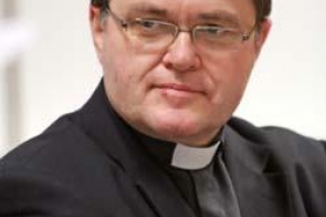 Ks. prof. Józef Budniak – duchowny katolicki i wykładowca akademicki, ubrany w klasyczną czarną sutannę z koloratką i marynarkę, z poważnym i zamyślonym spojrzeniem. Portret wykonany na jasnym tle.