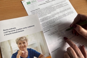 Widoczny jest formularz oraz broszura informacyjna dotycząca renty wdowiej, która wyjaśnia zasady łączenia renty rodzinnej z innymi świadczeniami. Na broszurze widnieje starsza, uśmiechnięta kobieta w niebieskiej bluzce. Obok dokumentów osoba z czerwonymi paznokciami wypełnia wniosek zielonym długopisem, wpisując dane w odpowiednich polach.