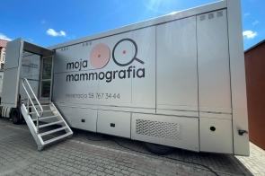 Mobilna pracownia mammograficzna w formie dużej, jasnej naczepy z logo „moja mammografia”, z metalowymi schodkami prowadzącymi do wejścia i numerem telefonu do rejestracji na boku pojazdu.