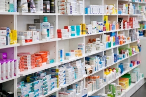 Kolorowe opakowania leków i suplementów ułożone na białych półkach w aptece tworzą uporządkowany, przejrzysty regał z szerokim wyborem produktów farmaceutycznych i higienicznych.