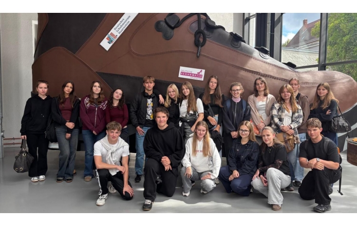 Grupa kilkunastu młodych ludzi,dziewcząt i chłopców,pozuje na tle ekspozycji - gigantycznego buta. 