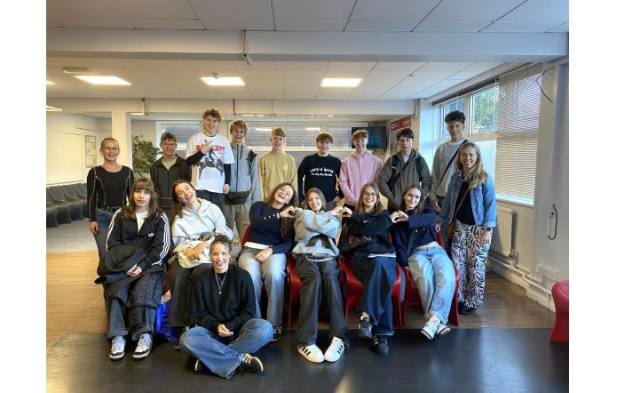 Siedemnaście uśmiechniętych młodych osób,dziewcząt i chłopców,pozujących w trzech rzędach.Sufit i ściany sali,na której się znajdują, są białe,a za nimi ściana jest mocno przeszklona.