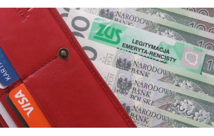 Czerwony skórzany portfel z widocznymi kartami płatniczymi w kieszonkach. Obok portfela leżą polskie banknoty oraz zielona legitymacja ZUS z napisem „Legitymacja emeryta-rencisty”.