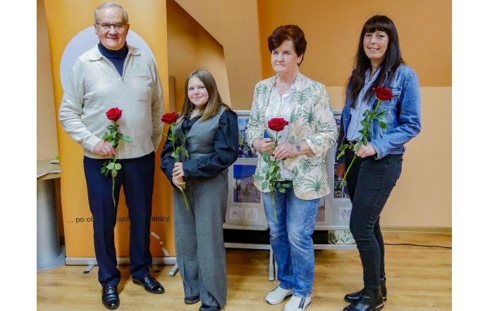 Laureaci konkursu „Selfie z marką Śląsk Cieszyński” stoją obok siebie z czerwonymi różami w dłoniach. Uśmiechnięci pozują do pamiątkowego zdjęcia na tle pomarańczowego baneru wydarzenia, symbolicznie zamykając jubileuszową edycję konkursu.