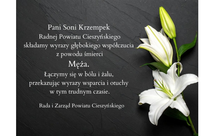 Czarny kamienny blat  z umieszczonym po lewej stronie tekstem kondolencyjnym, a po prawej dwie białe lilie– jedna rozwinięta i jedna w pąku. Tekst przekazuje wyrazy współczucia dla pani Soni Krzempek, radnej Powiatu Cieszyńskiego, z powodu śmierci męża. Pod wiadomością widnieje podpis: „Rada i Zarząd Powiatu Cieszyńskiego”.