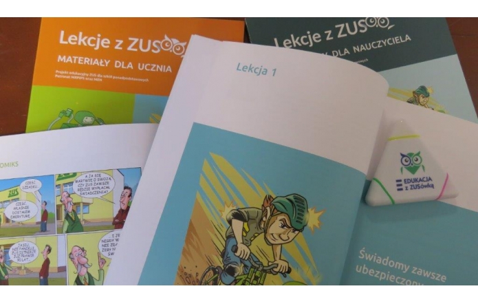 Rozsypane na biurku broszury „Lekcje z ZUS” — pomarańczowa dla ucznia i granatowa dla nauczyciela. Na wierzchu otwarta książeczka z napisem „Lekcja 1” i ilustracją chłopca jadącego na rowerze. Obok widać fragment komiksu oraz trójkątną, białą zakładkę z logo sowy „Edukacja z ZUSówką”.