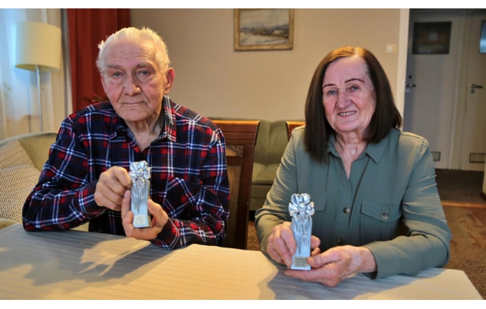 Na zdjęciu widzimy Helenę Bojko z mężem Janem. Każdy z nich trzyma w rękach Srebrną Cieszyniankę. Małżonkowie siedzą przy stole. Na ścianie w tle jest obraz o tematyce zimowej.