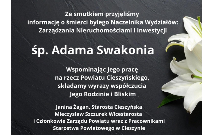 Czarny kamienny blat z delikatnie widocznym fragmentem białej lilii po prawej stronie oraz białym tekstem kondolencyjnym informującym o śmierci śp. Adama Swakonia, wraz z wyrazami współczucia od władz i pracowników Starostwa Powiatowego w Cieszynie.