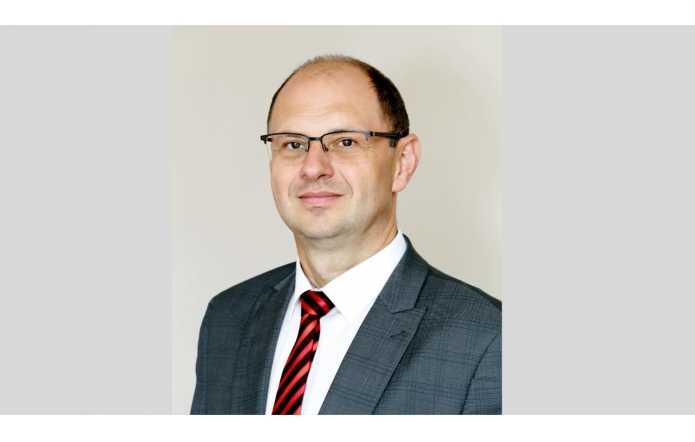 Nowy dyrektor Szpitala Śląskiego w Cieszynie Adam Śliż, ubrany w ciemną marynarkę, białą koszule i czerwowo-czarny krawat. Jest uśmiechnięty i ma założone okulary.